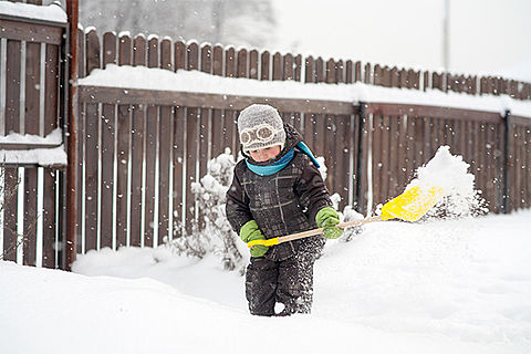 Ein kleines Kind versucht Schnee zu schaufeln. Noch sieht es wild entschlossen aus.