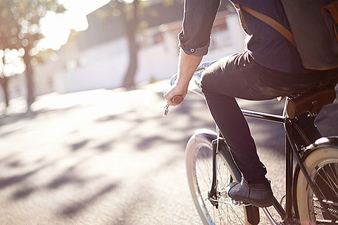Mann ist bei strahlendem Sonnenschein in der Stadt auf dem Fahrrad unterwegs, vermutlich auf dem Weg zur Arbeit
