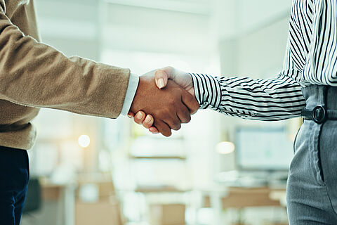 zu sehen sind zwei Personen in einem Büro, die sich die Hand geben