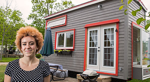 Eine lächelnde Frau steht vor ihrem Tiny House / Mobilheim.