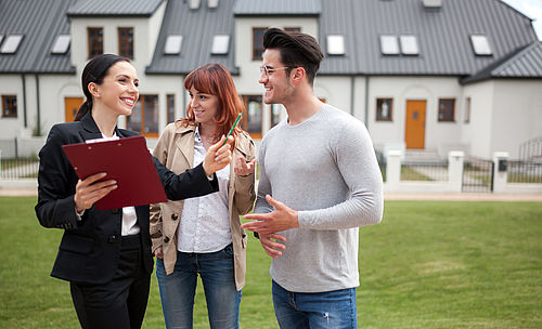 Ein junges Paar lässt sich von einer Immobilienmaklerin ein Haus zeigen.
