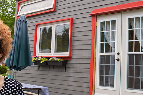 Eine lächelnde Frau steht vor Ihrem Tiny House / Mobilheim